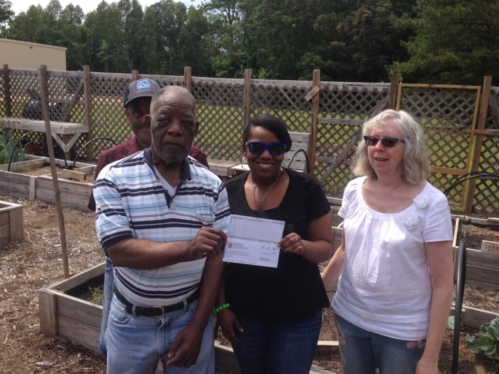 A group of people hold up a grant check in a community garden.